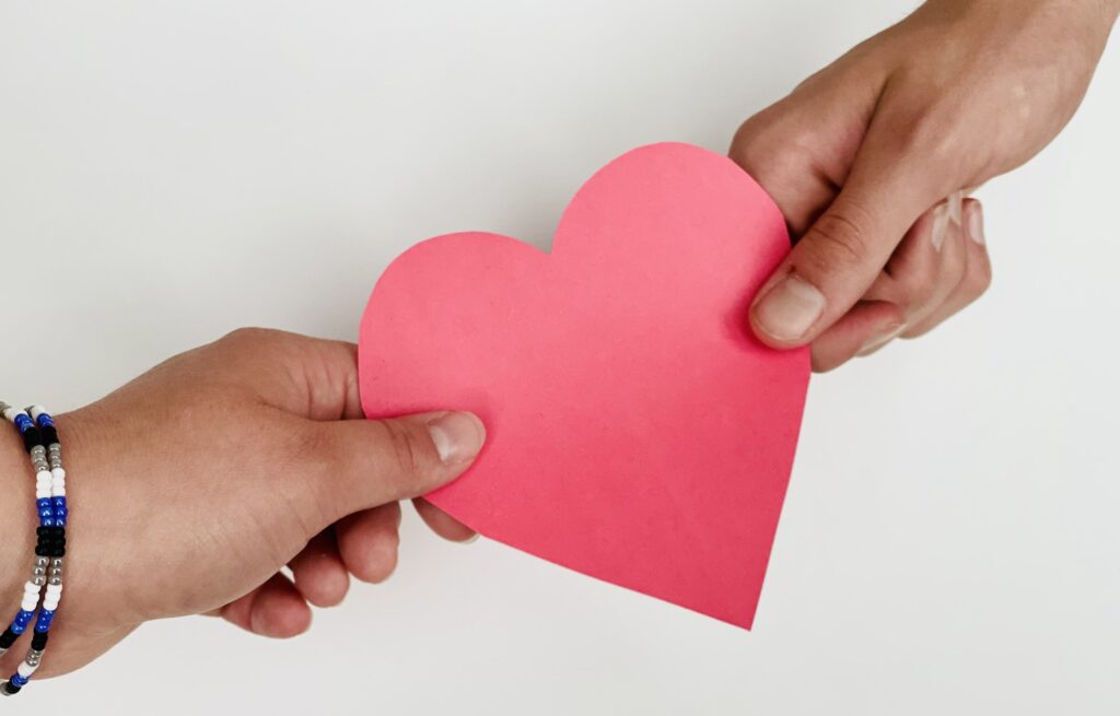 Red paper heart between male and female hands conceptual image share the love, background.